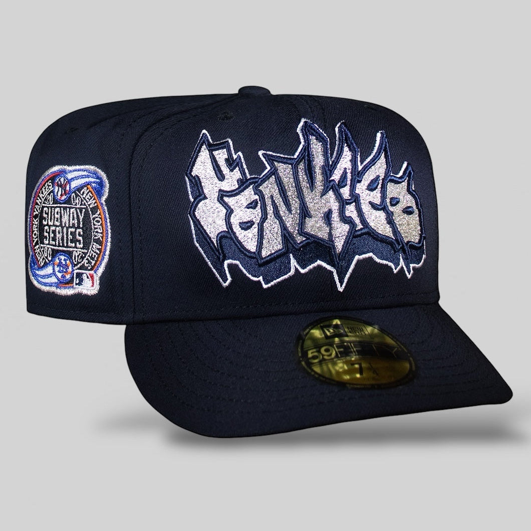 A navy blue New York Yankees baseball cap with a graffiti design on the front and a patch indicating the 2000 Subway Series on the side.